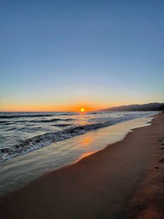 the sun is setting over the ocean at the beach with footprints in the sand and water