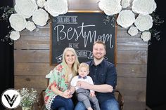 a man and woman sitting next to a baby in front of a chalkboard sign