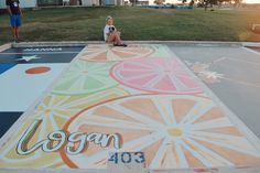 a person sitting on the ground in front of a painted area with oranges and lemons