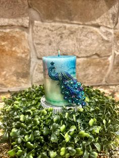 a candle that is sitting on some grass with a blue and green peacock painted on it