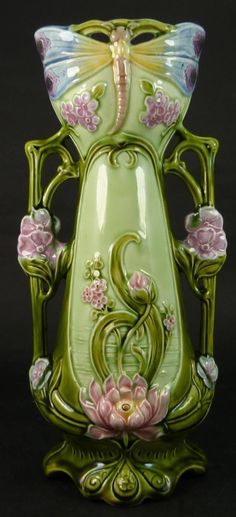 a green vase with pink flowers and a dragon on it's back side, sitting in front of a black background