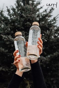 two people holding up empty water bottles in front of a tree with the words carry on it