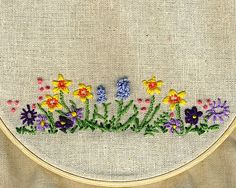 an embroidery project with flowers in the center and purple, yellow and orange flowers on the bottom