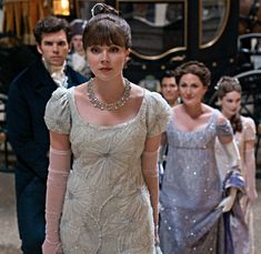 a woman in a white dress standing next to other people wearing formal clothing and accessories