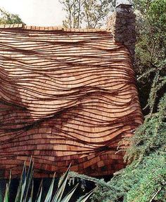 a building made out of bricks and wood in front of some trees with leaves on the roof