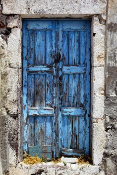 an old stone building with two blue doors and one has a flower in the middle