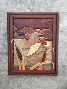 a wood carving of two ducks flying over reeds