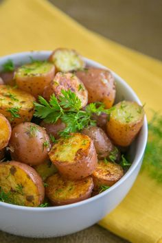 a bowl filled with potatoes and parsley on top of a yellow tablecloth covered table