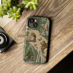 a cell phone case sitting on top of a wooden table next to a camera and plant