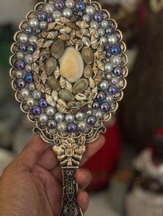 a close up of a person holding a small decorative object with pearls and seashells on it