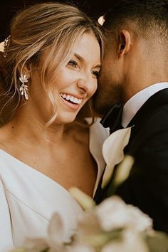 a bride and groom smile at each other as they pose for a wedding photo together