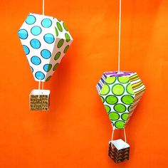 three paper hot air balloons hanging from strings on an orange wall with polka dot designs