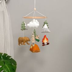 a mobile with animals and clouds hanging from it's sides next to a potted plant