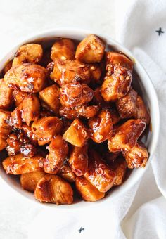 a white bowl filled with chicken and sauce on top of a table next to a napkin