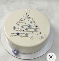 a white cake with a christmas tree decoration on the top and pearls around the edges