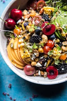 a white bowl filled with fruit and nuts on top of a blue tablecloth next to an avocado