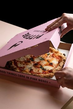 a person opening a pink box with a pizza in it on top of a table