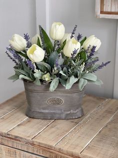 a flower pot sitting on top of a wooden table filled with white and purple flowers