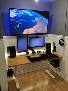 a computer desk with two monitors and speakers on it in front of a large screen