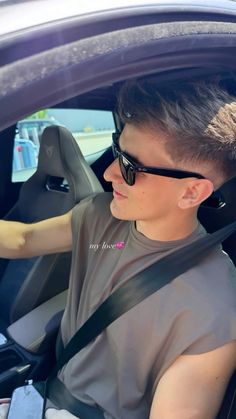 a young man sitting in the driver's seat of a car with sunglasses on