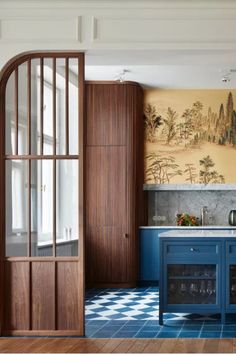 an open door leading to a kitchen with blue cabinets and counter tops, in front of a painting on the wall