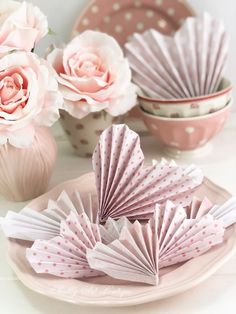 pink and white paper flowers in vases next to plates with folded origami fans on them