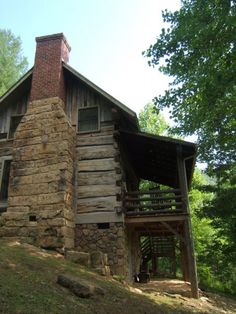 an old log cabin in the woods with a porch and stairs leading up to it