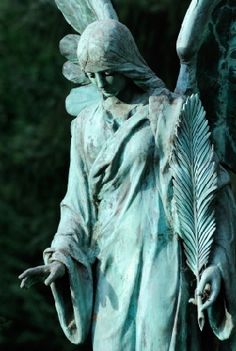 an angel statue holding a feather in its right hand with trees in the back ground behind it