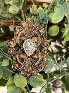 an ornate gold brooch with a diamond center surrounded by greenery and leaves on a white background