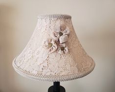 a lamp that is on a table with a flower in the middle and a lace shade over it