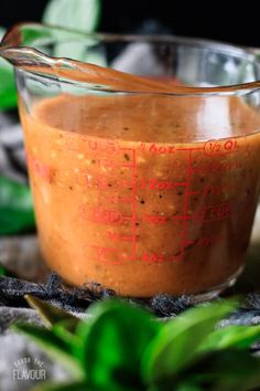 a glass measuring cup filled with brown sauce on top of green leafy plants and leaves