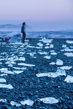 a man standing on top of a rocky beach next to ice floese covered in snow