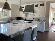 a large kitchen with white cabinets and marble counter tops, two pendant lights hanging over the island