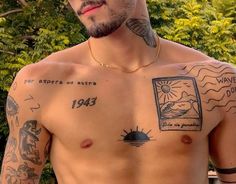 a man with tattoos on his chest standing in front of some trees and bushes looking at the camera