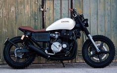 a white and black motorcycle parked in front of a wooden wall with metal bars on it