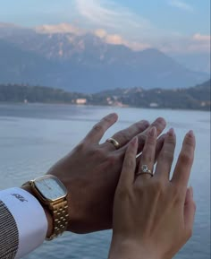 two hands holding each other with mountains in the back ground and water in the foreground