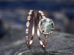 two wedding rings with an oval cut green stone surrounded by small white diamonds on top of a rock