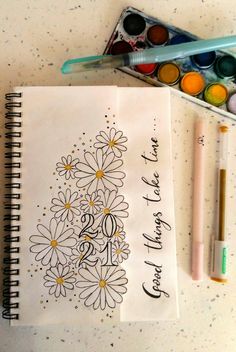 an open notebook with flowers on it next to markers and paint