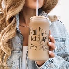 a woman holding a drink in her right hand and wearing a denim jacket with the words nail tech stay written on it