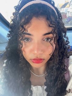 a woman with long curly hair wearing a headband and looking at the camera while sitting in a car