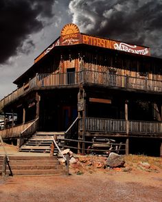 an old wooden building with stairs leading up to it and dark clouds in the background