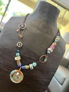 This is artisan-made work by me that I find one of my most soothing to experience in look, meaning, and thematic color warmth. I call this piece Joyous Self-determination. The pendant swirl draws to mind images of an earthy, earthly Celtic past while pulling us toward the evolution of self we call growth, learning, and self-understanding. It combines my handmade, kiln-fired ceramic elements with other artisan components as well as new and upcycled materials to create a one of a kind sort of myst Spiral Multicolor Necklace Gift, Bohemian Spiral Necklace As A Gift, Bohemian Spiral Necklace For Gift, Multicolor Spiral Necklace Gift, Bohemian Spiral Necklace As Gift, Bohemian Spiral Jewelry For Healing, Multicolor Copper Necklace, Unique Multicolor Copper Necklace, Artisan Spiral Wire Wrapped Necklaces