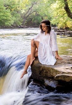 a woman sitting on top of a rock next to a river with water flowing over it