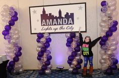 a woman standing in front of an entrance with purple and silver balloons on the side