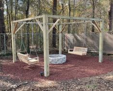 a swing set in the middle of a wooded area with two swings and a fire pit