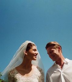 a man and woman standing next to each other in front of a blue sky with clouds