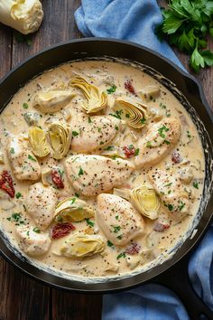 a skillet filled with chicken and artichokes on top of a wooden table