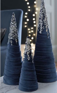 three small blue christmas trees sitting on top of a white marble table with lights in the background