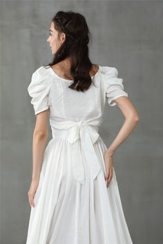 a woman is wearing a white dress with ruffled sleeves and a bow at the waist