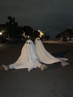 two white ghost figures sitting in the middle of a street at night with their heads turned to look like eyes